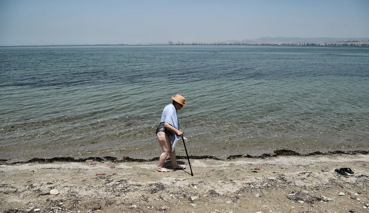 Seorang wanita berjalan di sepanjang pantai di Thessaloniki, Yunani utara (23/6/2021).  Yunani bersiap menghadapi gelombang panas pertama musim panas, mendorong suhu siang hari ke wilayah 40+ Celcius di banyak bagian negara. (AFP/ Sakis Mitrolidis)