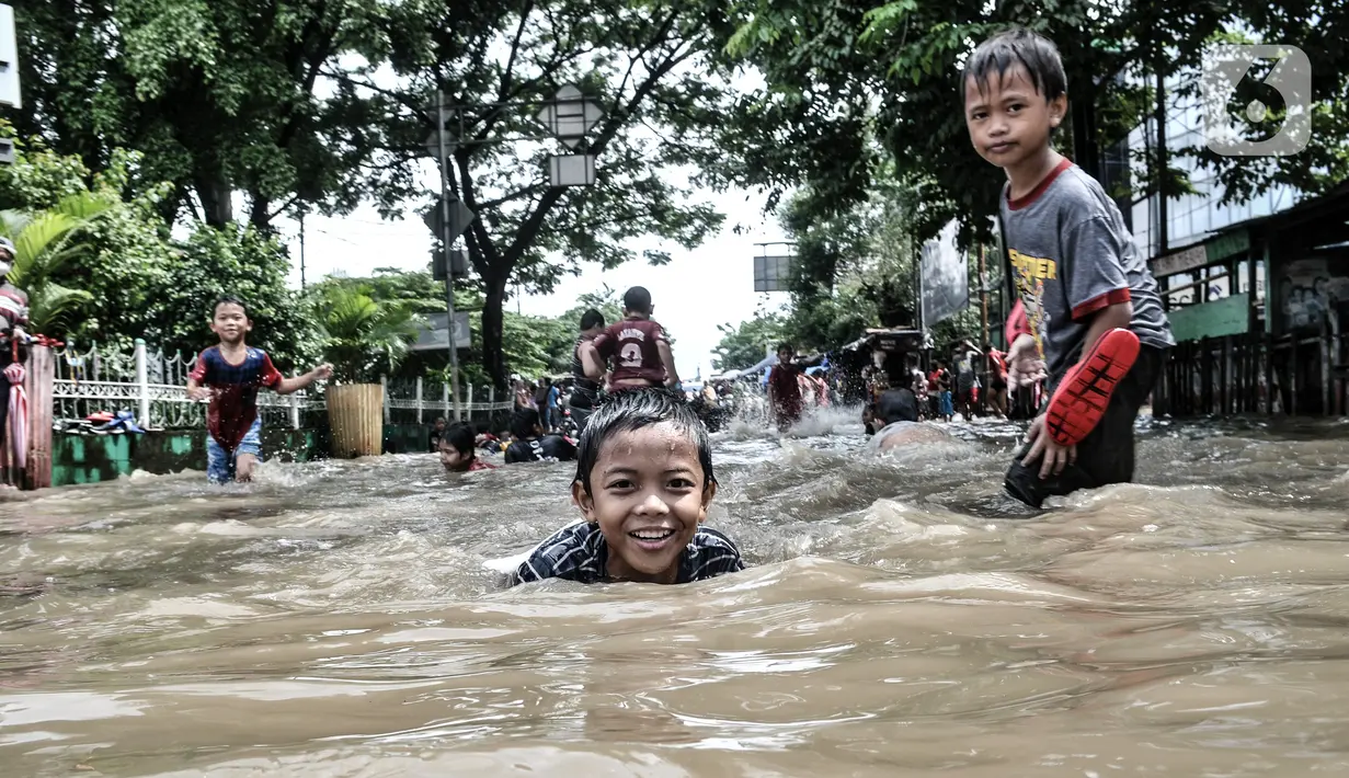 Anak-anak bermain air saat banjir menggenangi Jalan Jatinegara Barat, Jakarta, Senin (8/2/2021). Ketinggian air yang menggenangi Jalan Jatinegara Barat mencapai setinggi paha orang dewasa, sehingga menyebabkan kemacetan. (merdeka.com/Iqbal S. Nugroho)