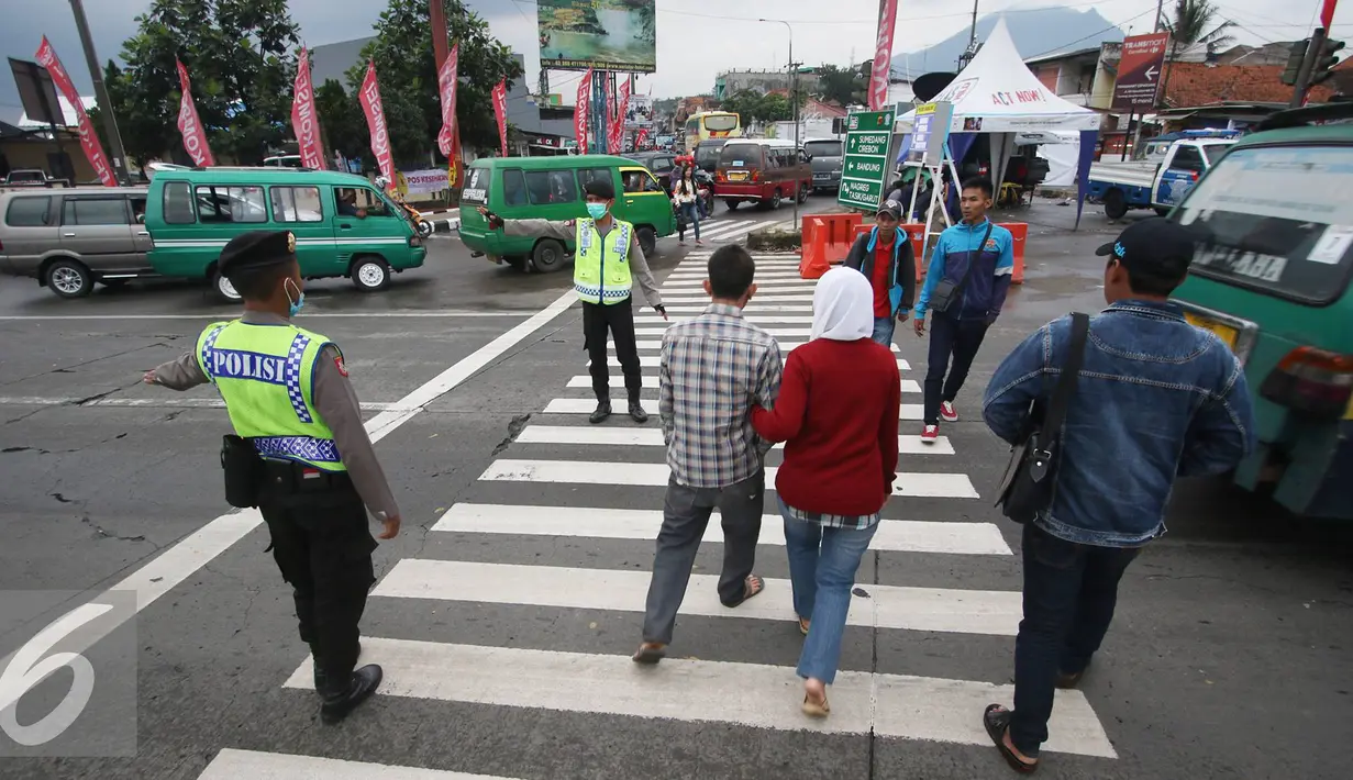 Petugas kepolisian membantu warga menyeberang jalan di Perempatan Cileunyi, Jawa Barat, Jumat (1/7). Mulai banyaknya kendaraan pemudik membuat petugas kepolisian membantu pejalan kaki yang ingin menyeberang. (Liputan6.com/Immanuel Antonius) 