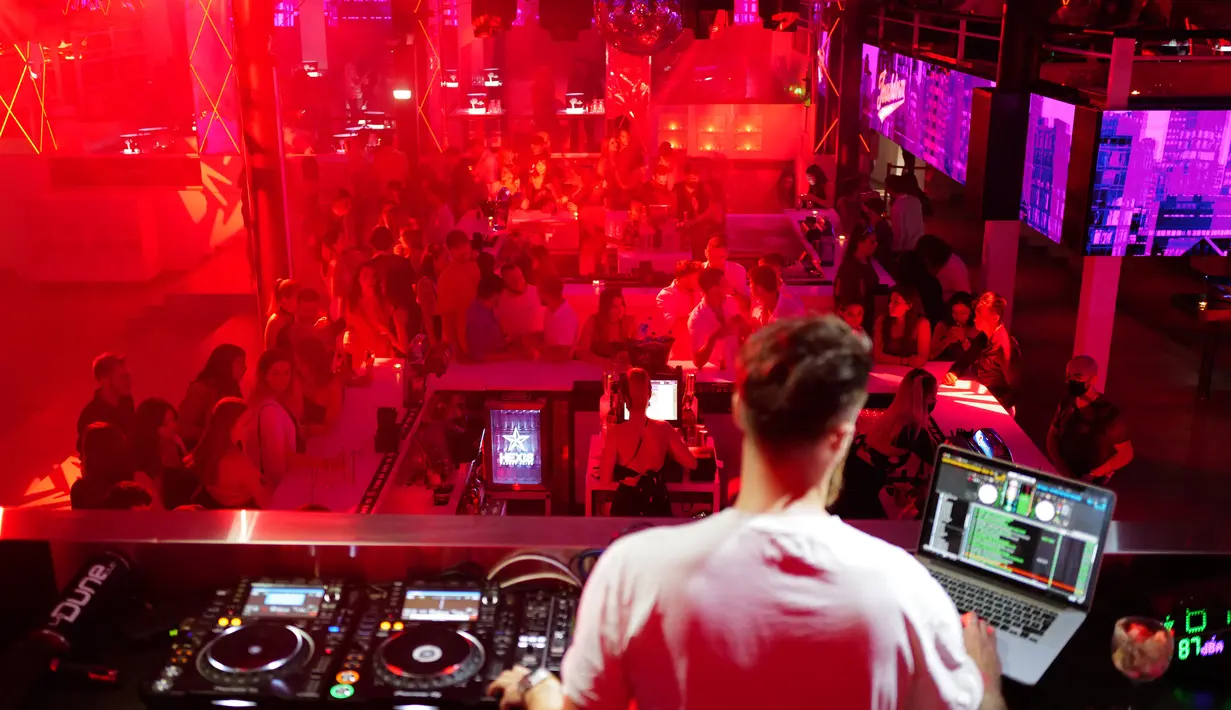 Seorang DJ menampilkan musik saat orang-orang menari di klub malam "La Dune" di kota selatan Prancis La Grande Motte, Sabtu (10/7/2021). (AFP/Sylvain Thomas)