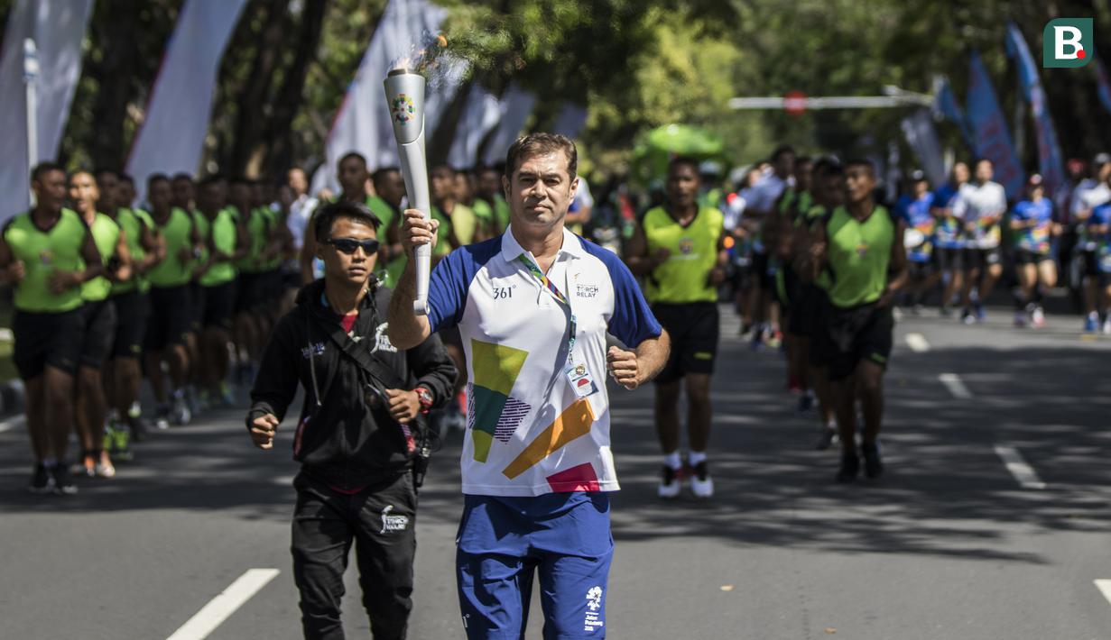 Pevoli legendaris Indonesia, Pascal Wilmar, berlari membawa obor Asian Games XVIII saat pawai di Denpasar, Bali, Selasa (24/7/2018). Sebanyak 53 kota di Indonesia akan dilalui oleh obor Asian Games. (Bola.com/Vitalis Yogi Trisna)