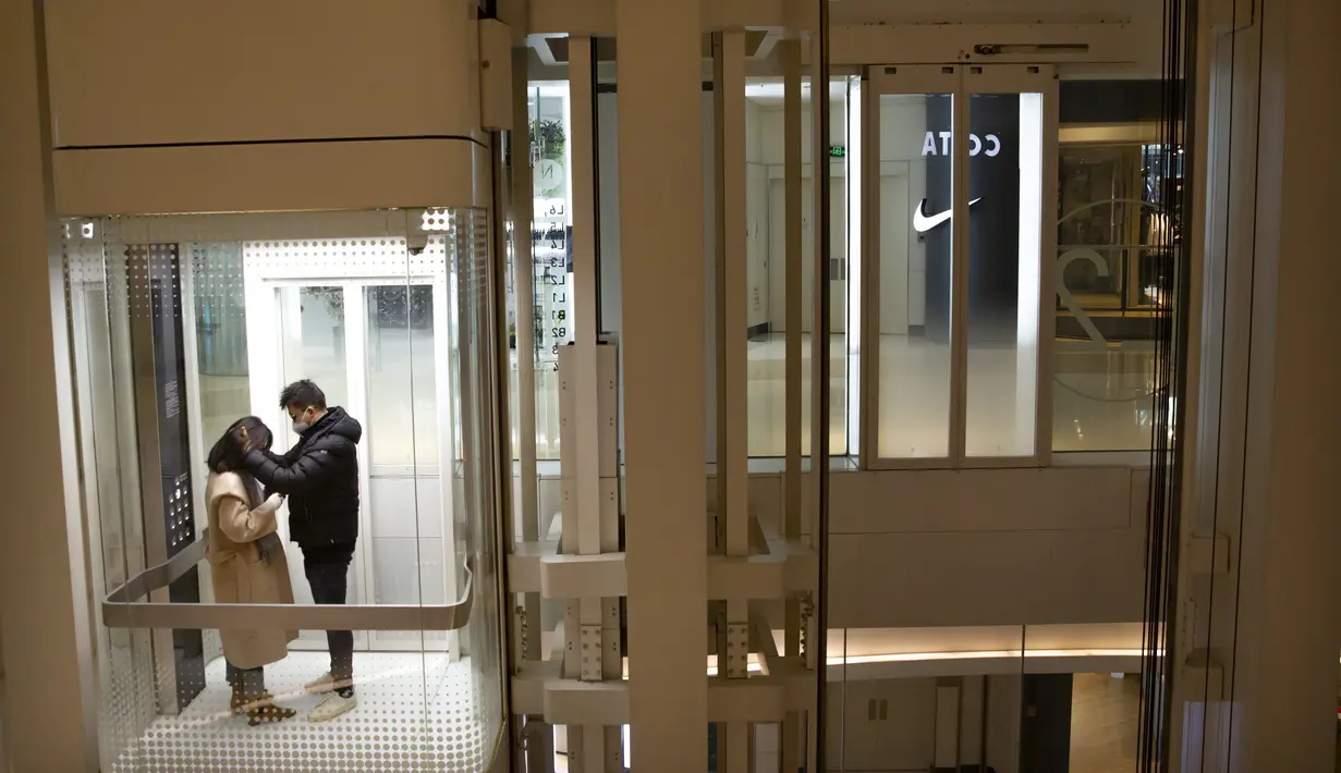 Pasangan memakai masker  naik lift di pusat perbelanjaan yang sepi pengunjung di Beijing (28/1/2020).  Mewabahnya virus corona membuat pusat perbelanjaan di Beijing, China, sepi pengunjung. (AP Photo/Mark Schiefelbein)
