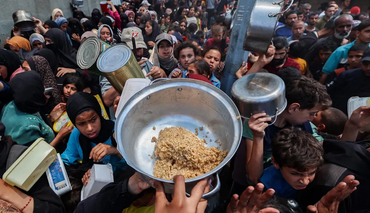 Warga Palestina berkumpul untuk menerima makanan hangat di titik distribusi makanan di kamp Nuseirat, Jalur Gaza Tengah pada 21 Mei 2025. (Eyad BABA/AFP)