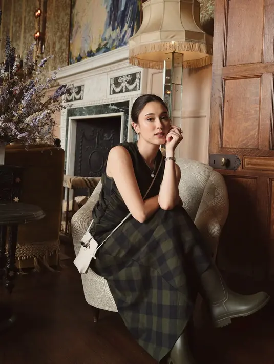 Di balik apron tersebut, Yasmin Napper kenakan sleeveless checkered long dress berbahan wol. Dipadu dengan boots tinggi dan sling bag putih [@yasminnaper]