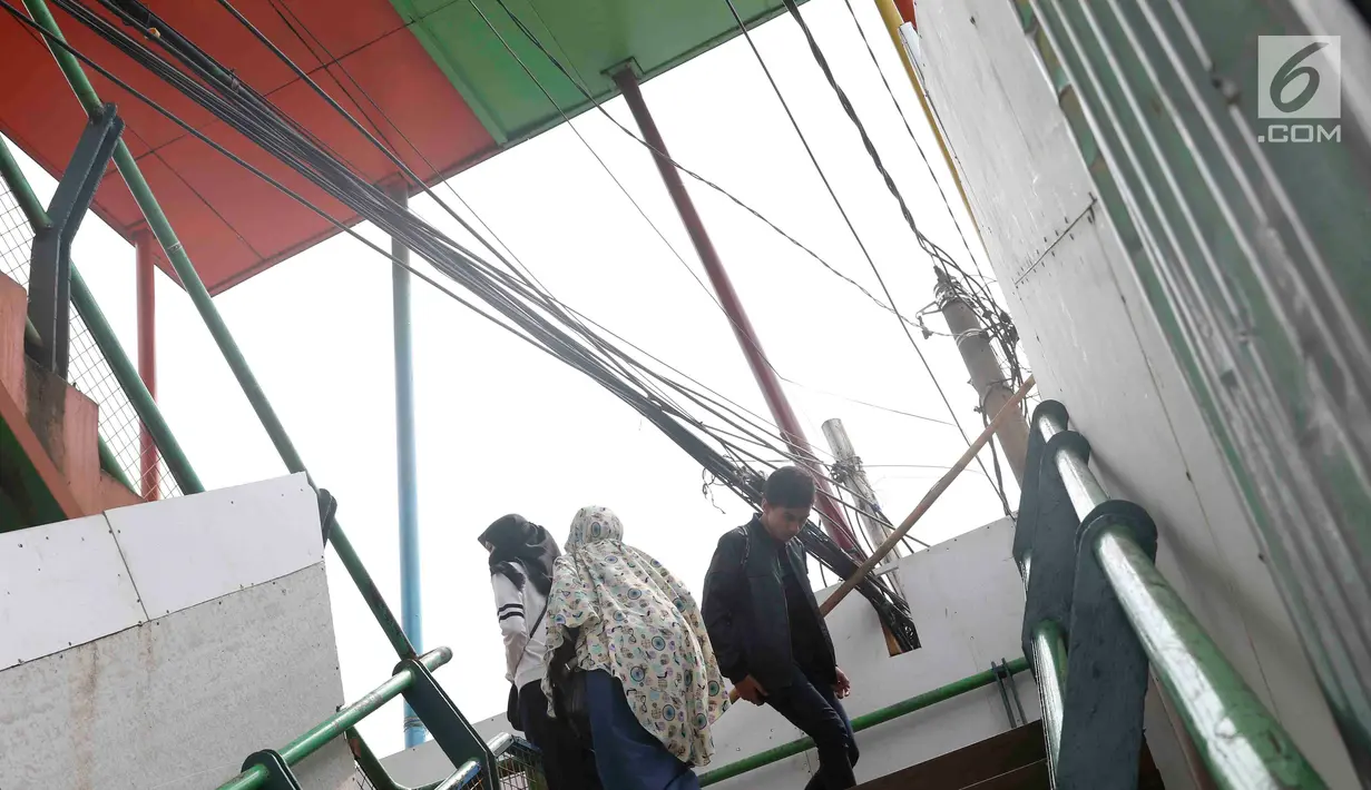 Pejalan kaki melintasi jembatan penyeberangan orang yang terhalang instalasi kabel di Depok, Jawa Barat, Sabtu (8/12). Selain mengganggu kenyamanan, keberadaan instalasi kabel semrawut tersebut membahayakan pejalan kaki. (Liputan6.com/Immanuel Antonius)