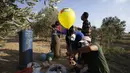 Warga Palestina bertopeng menempelkan alat peledak ke balon sebelum melepaskannya ke Israel di dekat kamp pengungsi al-Bureij di sepanjang perbatasan Israel-Gaza (12/8/2020). (AFP Photo/Mohammed Abed)