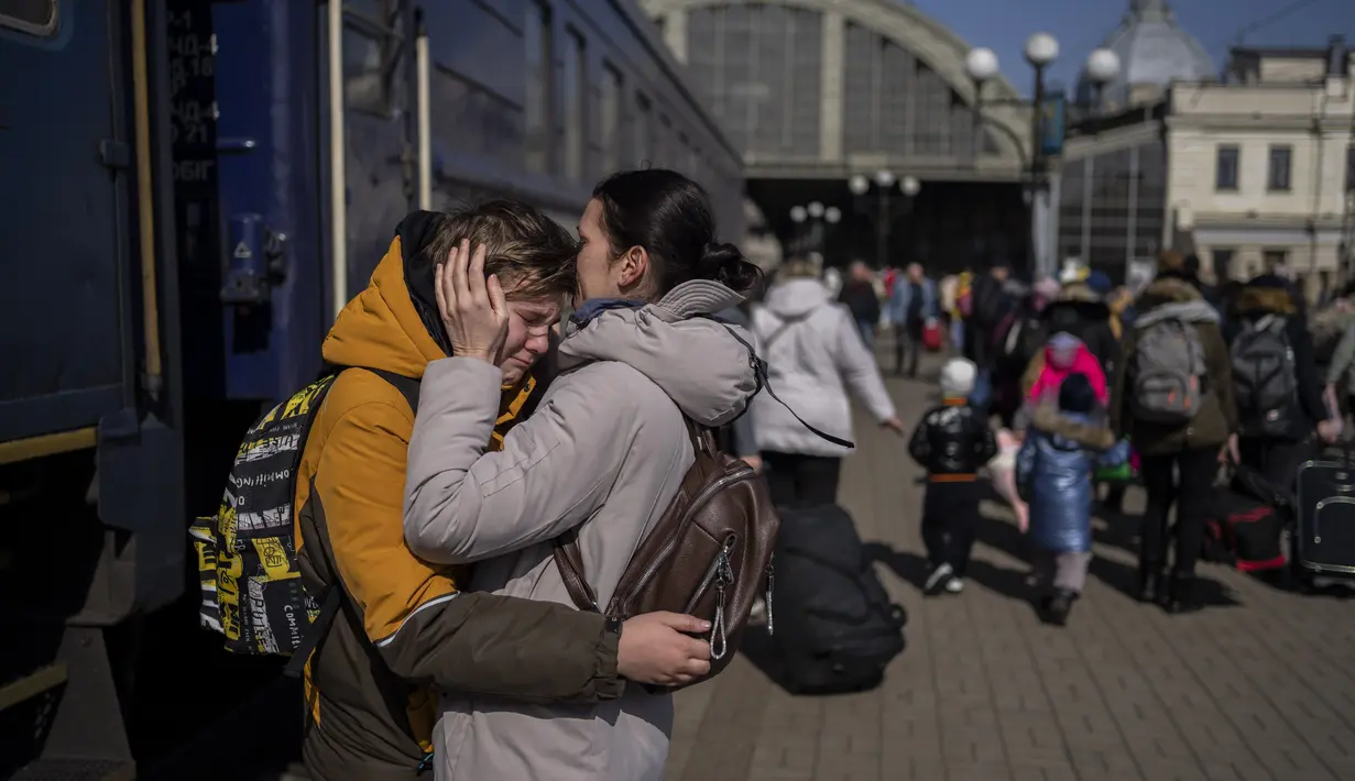 Seorang ibu memeluk putranya yang melarikan diri dari kota Mariupol yang terkepung dan tiba di stasiun kereta api di Lviv, pada 20 Maret 2022. Pada Hari 25 perang Rusia di Ukraina, kehidupan yang kacau, perpisahan yang pahit tertangkap dalam foto-foto Associated Press. (AP Photo/Bernat Armangue)