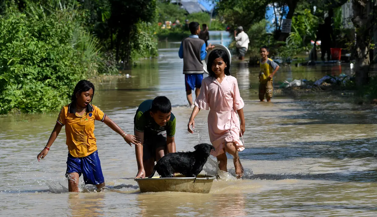 Anak-anak bermain di air banjir setelah hujan lebat di Phnom Penh, Kamboja (26/10/2021). Kementerian Sumber Daya Air dan Meteorologi telah mengeluarkan pemberitahuan pada hari Senin tentang situasi cuaca, mengkonfirmasikan risiko banjir di 14 ibu kota dan provinsi Kamboja. (AFP/Tang Chhin Sothy)