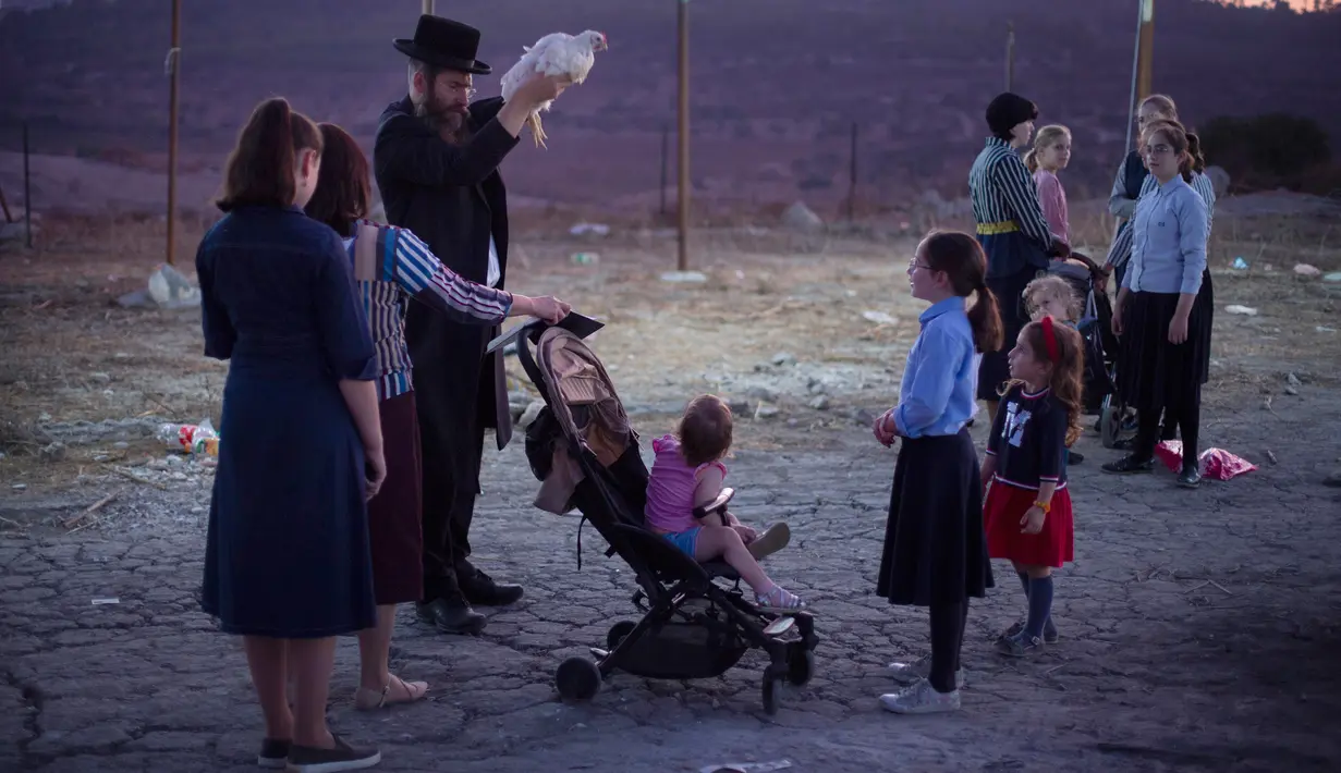 Seorang pria Yahudi Ultra-Ortodoks mengayunkan ayam di atas kepala keluarganya sebagai bagian dari ritual Kaparot di Beit Shemesh, Israel, Minggu (6/10/2019). Sebagian percaya, ritual Kaparot akan membebaskan mereka dari dosa-dosa yang ditransfer ke ayang yang dipotong. (AP/Oded Balilty)