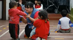 Noelia Garella bermain dengan muridnya di TK Jeromito, Argentina (24/10). Keinginan Noelia menjadi guru TK berawal dari masa kecil yang pahit saat dirinya ditolak masuk ke sebuah sekolah, bahkan dirinya disebut 'Monster'. (AFP Photo/Diego Lima)
