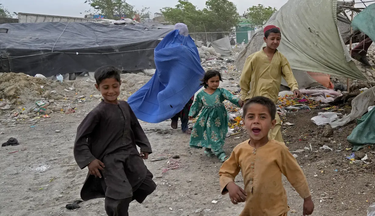 <p>Seorang perempuan yang mengenakan burqa dan anak-anaknya berjalan di depan rumah mereka di Kabul, Afghanistan, 8 Mei 2022. Taliban memerintahkan perempuan Afghanistan untuk mengenakan pakaian dari kepala hingga ujung kaki atau burqa tradisional di depan umum. (AP Photo/Ebrahim Noroozi)</p>