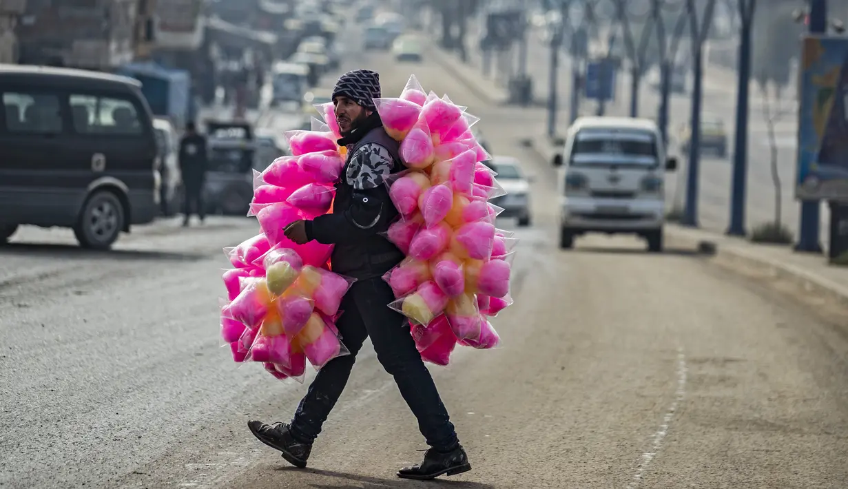 Seorang pedagang kaki lima yang menjual permen kapas melintasi jalan di kota Raqa, bekas ibu kota ISIS, di Suriah utara pada 20 Desember 2020. Raqqa menjadi saksi terusirnya anggota kelompok ekstremis oleh Pasukan Demokratik Suriah pada Oktober 2017 lalu. (Photo by Delil SOULEIMAN / AFP)