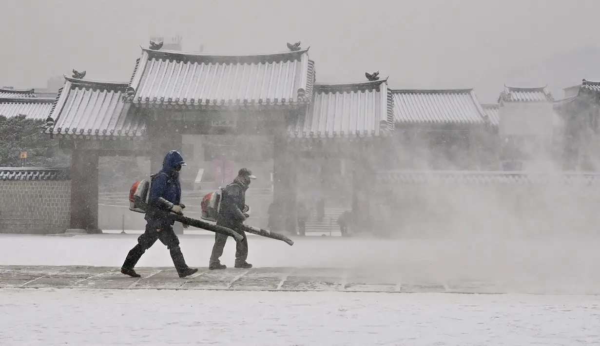 Pekerja menggunakan blower untuk membersihkan salju di Istana Gyeongbokgung di pusat kota Seoul (19/1/2022). Pemerintah metropolitan Seoul memobilisasi sekitar 9.000 pekerja dan 1.200 mobil penghapus salju dan peralatan lainnya. (AFP/Jung Yeon-je)