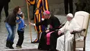 Seorang wanita menyusul anaknya yang menaiki panggung saat Paus Fransiskus menyampaikan audensi mingguan di Vatikan, Rabu (28/11). Sang ibu menjelaskan bahwa bocah 6 tahun tersebut  tunawicara dan berasal dari Argentina. (Vincenzo PINTO/AFP)