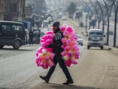 Seorang pedagang kaki lima yang menjual permen kapas melintasi jalan di kota Raqa, bekas ibu kota ISIS, di Suriah utara pada 20 Desember 2020. Raqqa menjadi saksi terusirnya anggota kelompok ekstremis oleh Pasukan Demokratik Suriah pada Oktober 2017 lalu. (Photo by Delil SOULEIMAN / AFP)