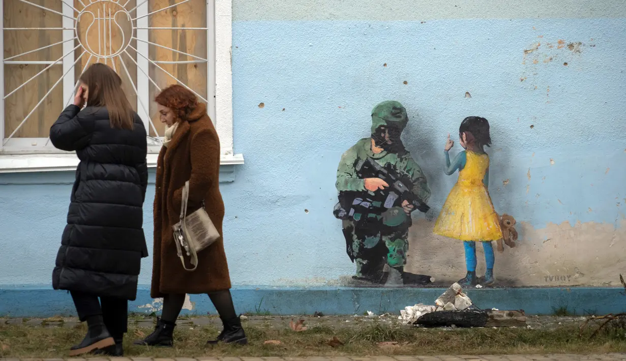 Orang-orang melewati karya seni dari seniman jalanan terkenal TvBoy yang dibuat pada dinding rumah budaya yang rusak berat akibat serangan Rusia di Kota Irpin, Ukraina, 30 Januari 2023. Karya seni yang dibuat untuk menghormati para korban perang Rusia-Ukraina tersebut mengandung pesan kelahiran kembali dan harapan serta berharap agar konflik segera berakhir. (AP Photo /Efrem Lukatsky)
