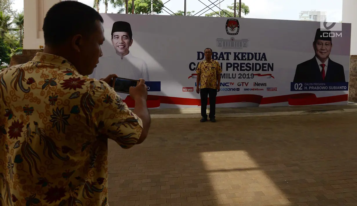 Seorang pria foto di depan baliho debat Capres kedua di Hotel Sultan, Jakarta, Jumat (15/2). KPU mengusung materi debat kedua Capres 2019 mengangkat tema energi, pangan, infrastruktur, sumber daya alam, dan lingkungan hidup. (Merdeka.com/Imam Buhori)