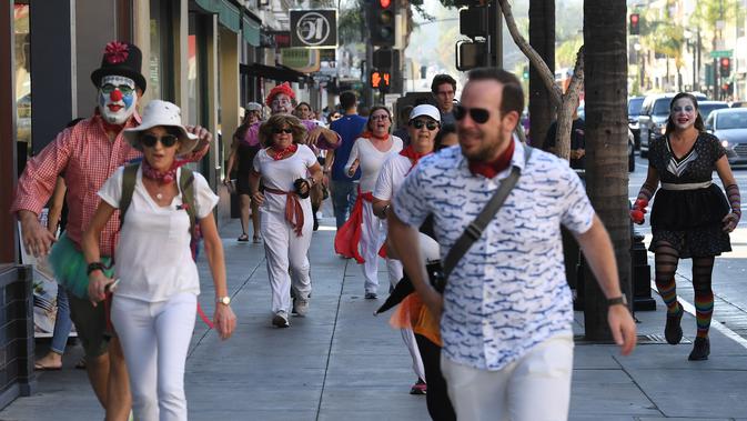 Pejalan kaki berlarian dikejar kawaan badut dalam 'Running of the Clowns' di Pasadena, California pada 21 Oktober 2018. Lari dikejar kawanan badut ini merupakan parodi yang mengolok-olok lomba dikejar banteng di Pamplona, Spanyol. (Mark RALSTON/AFP)
