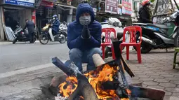 Seorang pria menghangatkan diri di depan kayu bakar saat hari musim dingin di Hanoi, Vietnam, Jumat (8/1/2021). Vietnam tahun ini diperkirakan mengalami musim dingin yang lebih dingin dari biasanya ketika suhu permukaan laut Samudra Pasifik turun, membentuk fenomena La Nina. (Nhac NGUYEN/AFP)