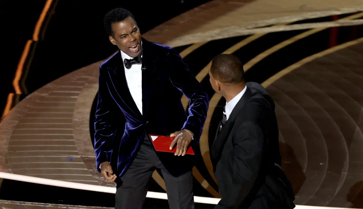 Will Smith (kanan) memukul presenter Chris Rock di atas panggung Piala Oscar 2022 saat penghargaan untuk film dokumenter terbaik di Dolby Theatre, Minggu (27/3/2022). Will Smith merasa lawakan sang komedian terkait istrinya, Jada Pinkett Smith keterlaluan. (Neilson Barnard/Getty Images/AFP)