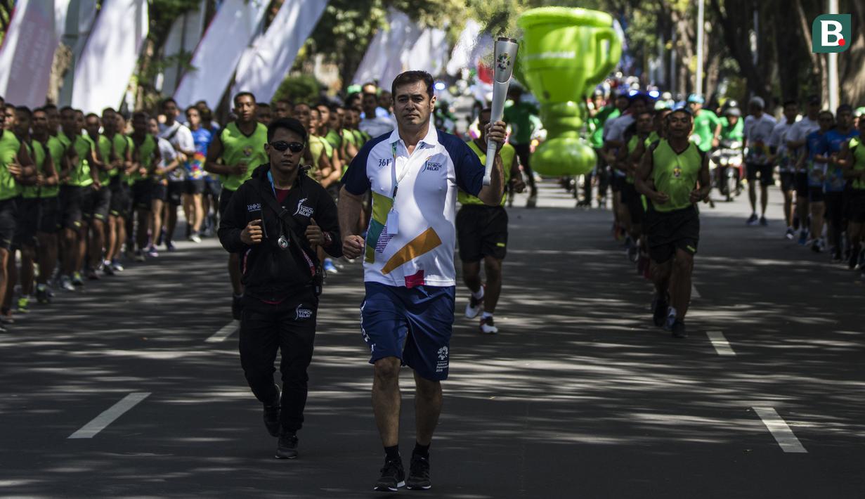 Pevoli legendaris Indonesia, Pascal Wilmar, berlari membawa obor Asian Games XVIII saat pawai di Denpasar, Bali, Selasa (24/7/2018). Sebanyak 53 kota di Indonesia akan dilalui oleh obor Asian Games. (Bola.com/Vitalis Yogi Trisna)