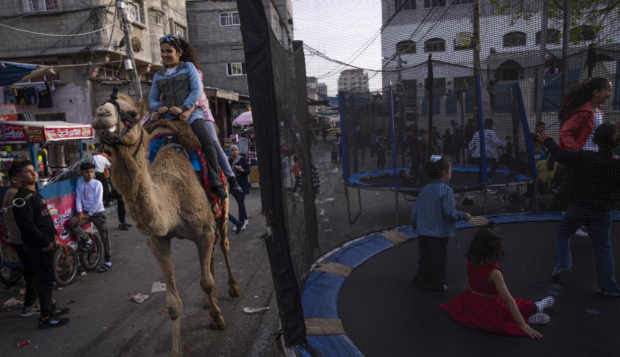 Gadis-gadis Palestina menunggang unta saat mereka merayakan festival Idul Fitri, menandai akhir bulan puasa Ramadhan di kamp pengungsi al-Shati, Jalur Gaza barat, Sabtu, 22 April 2023. (AP Photo/Fatima Shbair)
