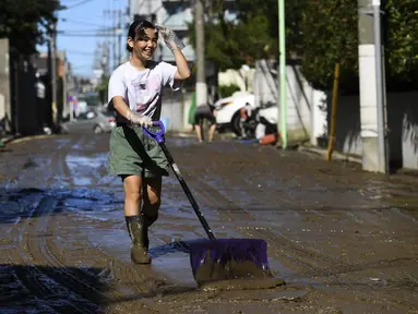 Seorang anak membersihkan lumpur dari jalan setelah banjir surut di Kawasaki, Minggu (13/10/2019). Topan dahsyat Hagibis yang menerjang sejumlah wilayah di Jepang menyebabkan banjir di beberapa lokasi. (Photo by WILLIAM WEST / AFP)