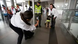 Seorang wanita berfoto dengan anjing polisi ahli pengendus narkoba, Sombra di bandara El Dorado, Bogota, 26 Juli 2018. Anjing itu diburu geng narkoba Kolombia, Urbenos karena berhasil menggagalkan penyelundupan 10 ton kokain miliknya (AP/Fernando Vergara)