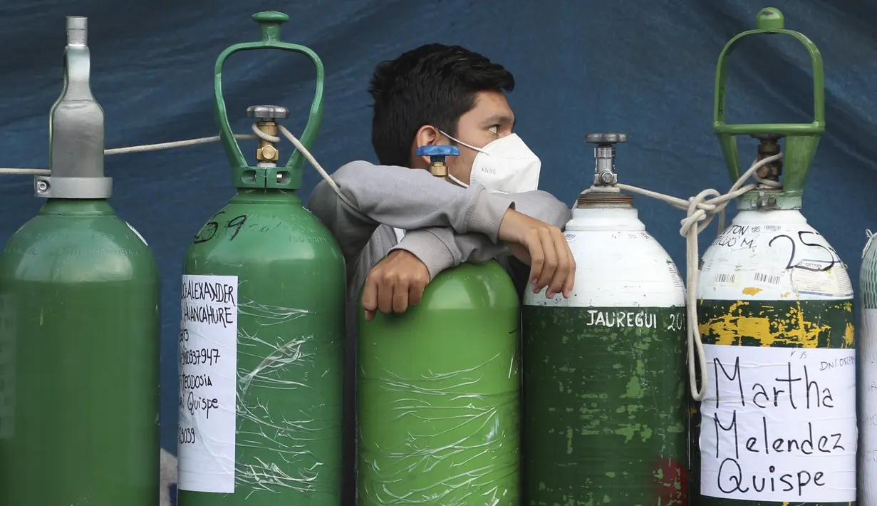 Seorang pemuda bersandar pada tabung oksigennya yang kosong saat menunggu toko isi ulang dibuka di lingkungan San Juan de Lurigancho di Lima, Peru, Senin (22/2/2021). Kekurangan oksigen medis untuk merawat pasien COVID-19 terus menjadi norma nasional. (AP Photo/Martin Mejia)