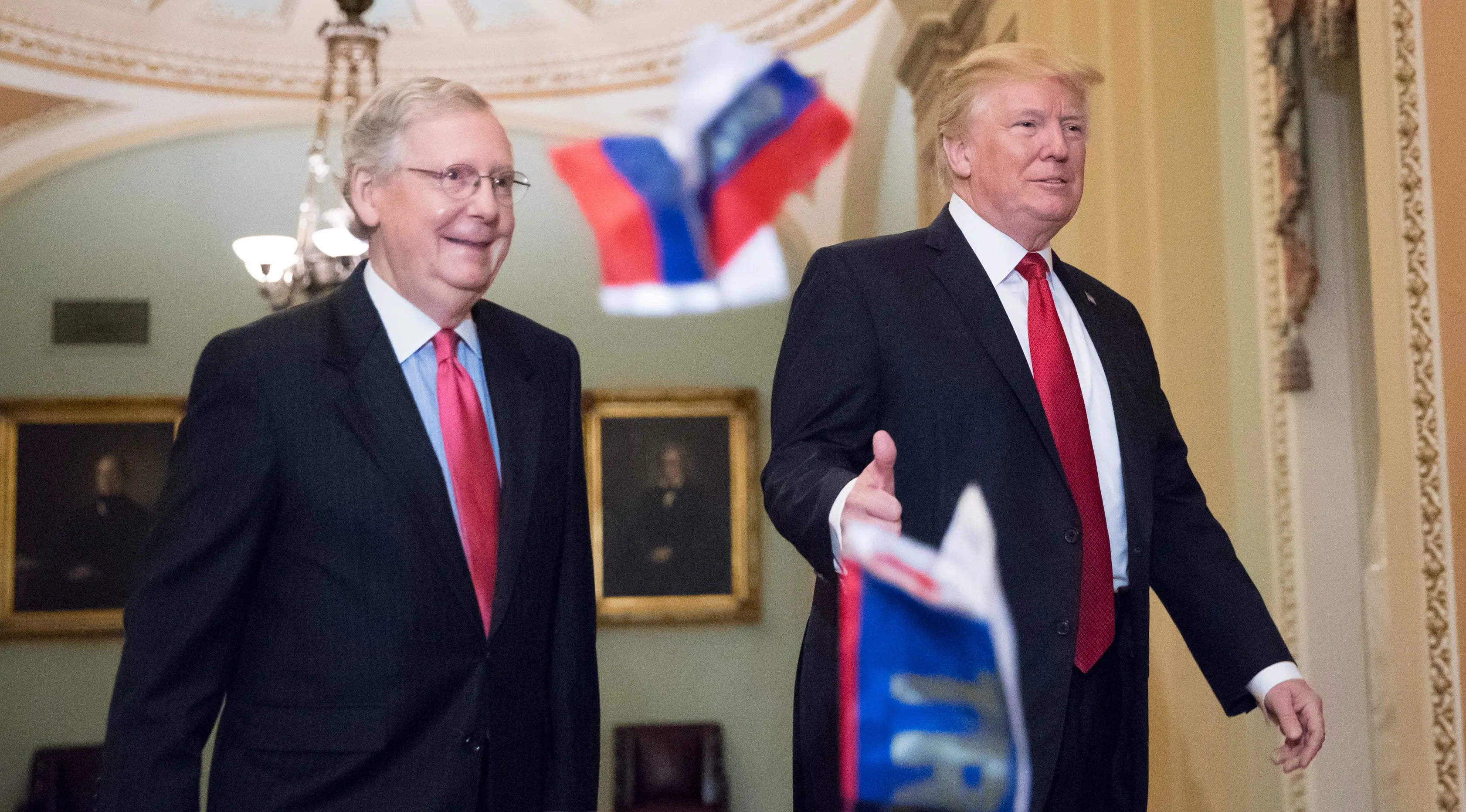 Bendera Rusia dilemparkan ke arah Presiden AS, Donald Trump yang berjalan bersama senator Mitch McConnel di Capitol Hill, Washington DC, Selasa (24/10). Pada saat itu, Trump hendak hadir di acara makan siang rutin dengan senator. (AP/J. Scott Applewhite)