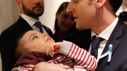 Presiden Prancis Emmanuel Macron menggendong seorang anak saat mengunjungi Graffiti's- Association Le Moulin Vert di Normandia, Prancis (5/4). Pada kunjungannya Presiden Emmanuel Macron berinteraksi dengan anak-anak autis.  (AP / Christophe Ena, Pool)