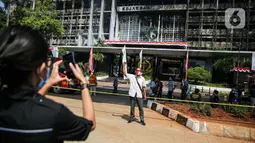Seorang pria berfoto dengan latar belakang gedung utama Kejaksaan Agung RI yang terbakar di Jalan Sultan Hasanuddin, Jakarta, Minggu (23/8/2020). Banyak warga yang memadati Jalan Hasanuddin untuk melihat langsung kondisi gedung Kejaksaan Agung yang hangus dilalap api. (Liputan6.com/Faizal Fanani)