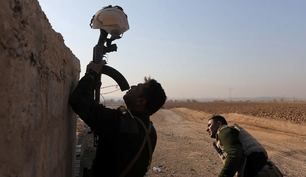 Seorang tentara Irak menggunakan senapan untuk menahan helm sebagai umpan dalam bentrokan dengan militan ISIS di Al-Qasar, Tenggara Mosul, Irak (28/11). (REUTERS/Goran Tomasevic)