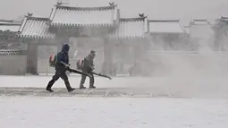 Pekerja menggunakan blower untuk membersihkan salju di Istana Gyeongbokgung di pusat kota Seoul (19/1/2022). Pemerintah metropolitan Seoul memobilisasi sekitar 9.000 pekerja dan 1.200 mobil penghapus salju dan peralatan lainnya. (AFP/Jung Yeon-je)