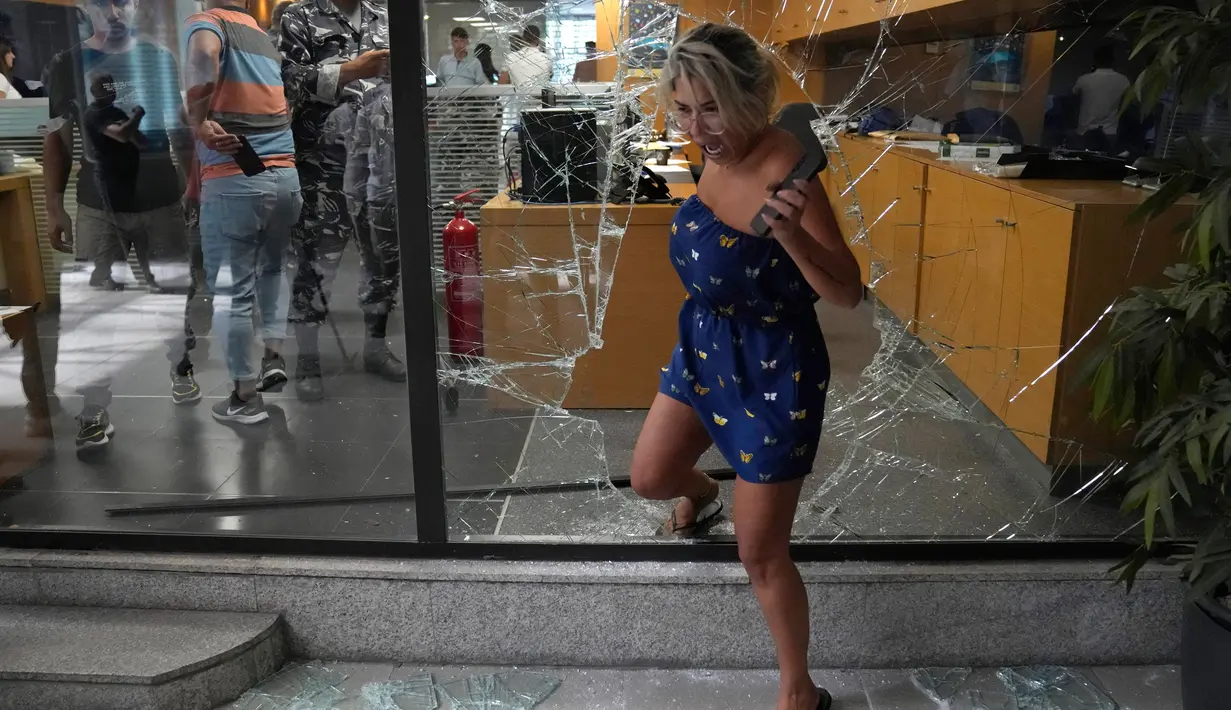Seorang karyawan bank keluar dari bank melalui jendela yang dirusak oleh penyerang, Beirut, Lebanon, Rabu (14/9/2022). Seorang wanita bersenjata dan belasan aktivis masuk ke cabang bank Beirut mengambil alih $13.000 dari tabungannya yang ditahan oleh bank tersebut. (AP Photo/Hussein Malla)