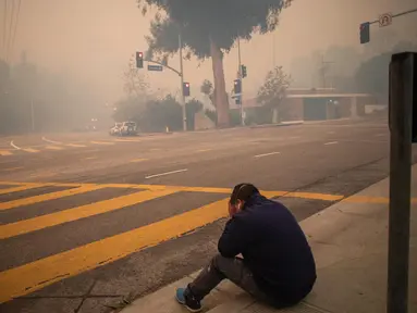 Orang-orang berhenti sejenak untuk mengambil nafas saat mereka mengungsi di sepanjang Sunset Boulevard saat kebakaran berkobar di tengah-tengah badai angin di kawasan Pacific Palisades, Los Angeles, California, Amerika Serikat pada 7 Januari 2025. (Apu Gomes/Getty Images North America/Getty Images via AFP)