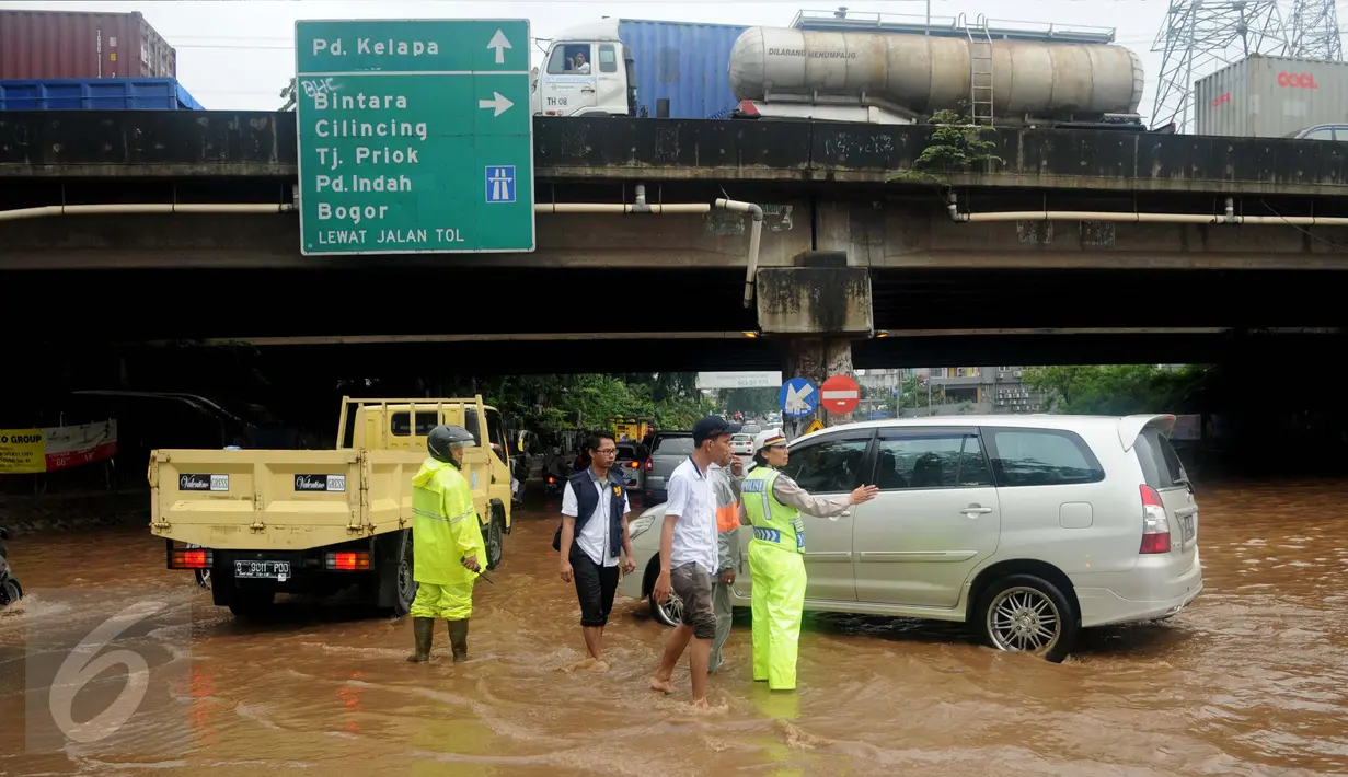 Petugas polisi mengatur lalu lintas di tengah banjir yang melanda Jalan Raya Kalimalang, Caman, Bekasi, Senin (20/2). Banyak kendaraan yang mogok karena nekat menorobos banjir dengan ketinggian sekitar 80 cm. (Liputan6.com/Gempur M Surya)