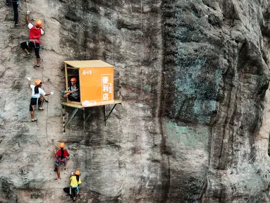 Sejumlah orang memanjat tebing melewati toko serba ada yang menempel di dinding tebing di Pingjiang di provinsi Hunan, China (25/4). Toko ini menjual minuman dan makanan untuk para pemanjat tebing yang melintas. (AFP Photo/China Out)