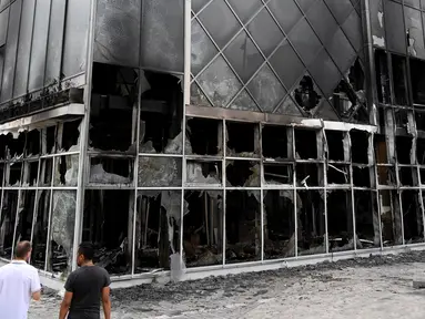Dua pria melihat fasad Hotel du ville yang hangus dan terbakar di Garges-les-Gonesse, utara Paris, menyusul kerusuhan dua hari setelah seorang remaja 17 tahun ditembak di dada oleh polisi dari jarak dekat di Nanterre, pinggiran barat Paris, pada 29 Juni 2023. (Photo by Bertrand GUAY / AFP)