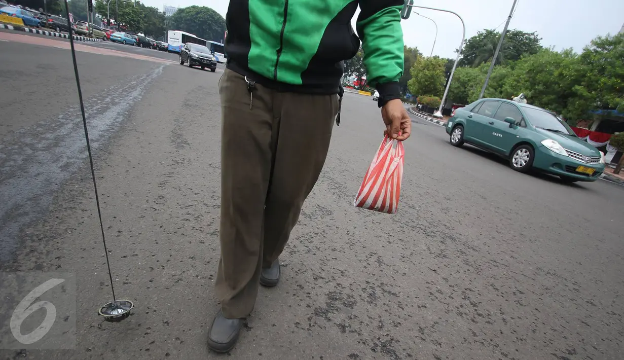 Pengendara Gojek bernama Ari mencari ranjau paku yang berserakan di sekitar Istana Negara, Jakarta, Minggu (14/8). Meskipun tak dibayar, Ari berinisiatif untuk mengumpulkan ranjau paku yang merugikan pengendara tersebut. (Liputan6.com/Immanuel Antonius)