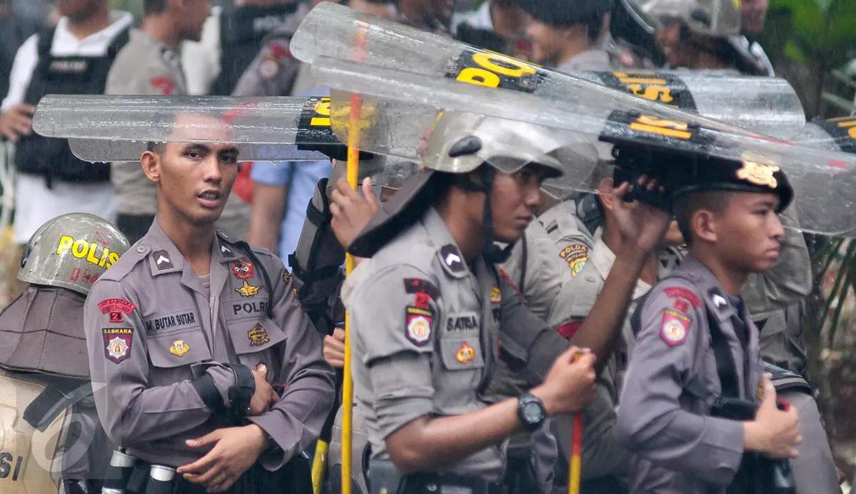 Petugas kepolisian menggunakan tameng untuk berteduh dari hujan saat menjaga aksi Hari Buruh di Jalan Medan Merdeka, Jakarta, Senin (1/5). (Liputan6.com/ Yoppy Renato)