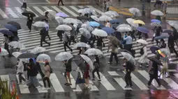 Para komuter yang mengenakan payung menyeberangi jalan saat  hujan yang dibawa oleh Topan Mindulle di Tokyo, Jepang, Jumat (1/10/2021). Topan Mindulle sedang bergerak di lepas pantai Jepang. (AP Photo/Kiichiro Sato)