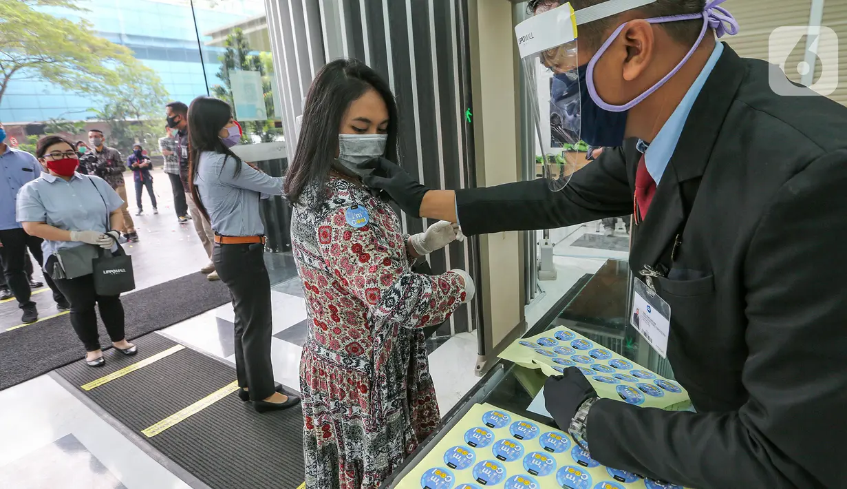 Petugas menempel stiker ke pengunjung usai cek suhu tubuh di Lippo Mall Puri, Jakarta, Senin (15/6/2020). Lippo Malls di wilayah Jakarta kembali beroperasi pada pukul 12.00 – 20.00 WIB dengan menyiapkan protokol kesehatan guna mencegah penyebaran Covid-19. (Liputan6.com/Fery Pradolo)