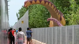 Orang-orang berhenti untuk mengambil foto replika dinosaurus seukuran aslinya yang dipajang di sepanjang "Changi Jurassic Mile" jalan santai di Singapura (13/10/2020). Singapura membangun replika-replika dinosaurus di jalur menunju bandara Changi. (AFP/Roslan Rahman)