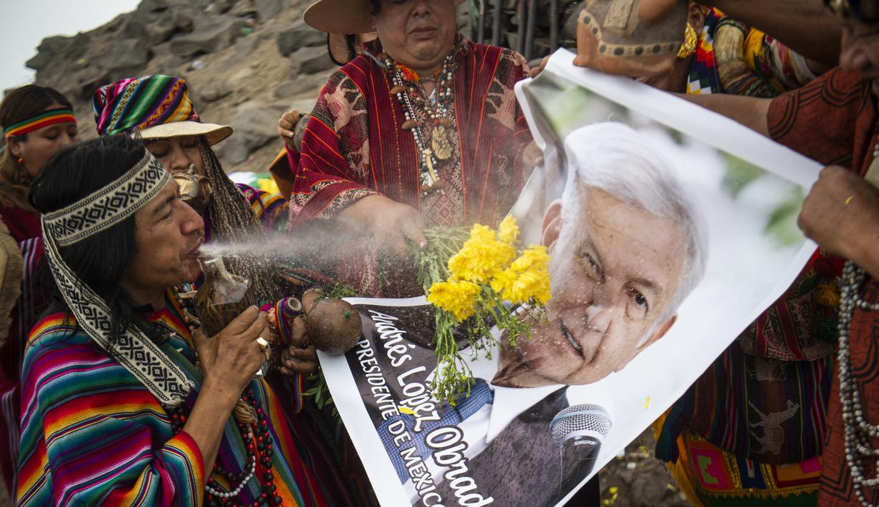 Dukun Peru menyemprotkan air ke foto Presiden Meksiko Andres Manuel Lopez Obrador saat memberikan prediksi untuk 2022 dalam ritual tradisional sebelum Malam Tahun Baru di bukit San Cristobal di Lima, Peru  (29/12/2021). (AFP/Ernesto Benavides)