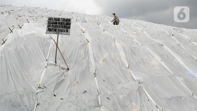 Pemulung melewati gunungan sampah yang ditutupi plastik besar di Tempat Pembuangan Akhir (TPA) Cipayung, Depok, Jawa Barat, Selasa (21/1/2020). Pemasangan plastik tersebut dilakukan sejak kemarin untuk mengurangi bau tak sedap di musim hujan sekaligus mengurai sampah. (merdeka.com/Arie Basuki)
