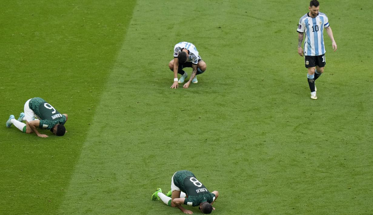 Penyerang Argentina Lionel Messi meninggalkan lapangan saat bek Arab Saudi Mohammed Al-Burayk dan rekan setimnya Abdulelha Al-Malki berselebrasi dengan cara sujud pada laga pembuka Grup C Piala Dunia 2022 Qatar di Lusail Iconic Stadium, Lusail, Selasa (22/11/2022). Argentina kalah 1-2 dari Arab Saudi. (AP Photo/Luca Bruno)
