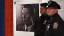 Dua petugas NYPD berdiri dekat instalasi seni yang memajang gambar David Bowie di stasiun kereta bawah tanah Broadway-Lafayette, New York City, 19 April 2018. Instalasi seni yang berlangsung hingga 13 Mei mendatang. (ANGELA WEISS/AFP)