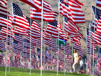 Seorang wanita dan anak melewati pameran bendera AS untuk peringatan 20 tahun serangan 9/11 di Pepperdine University di Malibu, Rabu (8/9/2021). Selama 14 tahun, universitas itu memperingati tragedi 11 September 2001 dengan mengibarkan sekitar 3.000 bendera Amerika. (Frederic J. BROWN/AFP)