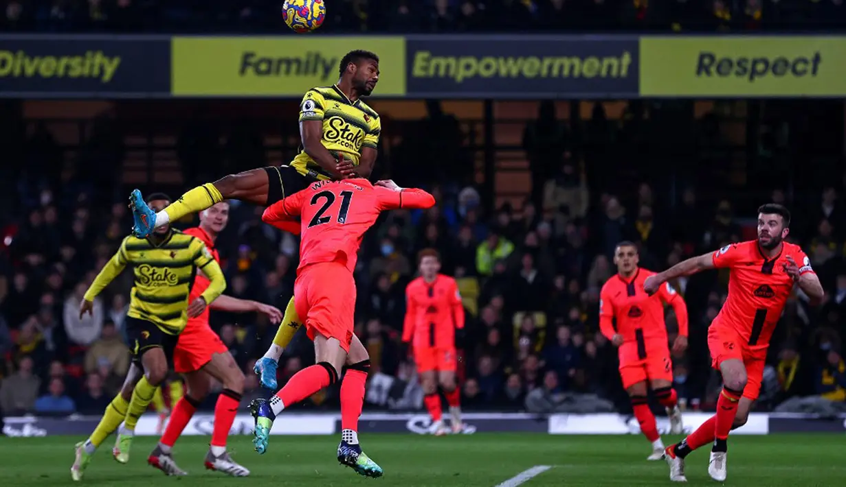 Pemain Watford Emmanuel Dennis melompat di atas pemain Norwich City Brandon Williams untuk menyundul bola dari umpan silang pada pertandingan sepak bola Liga Inggris di Vicarage Road Stadium, Watford, Inggris, Sabtu (22/1/2022). Norwich City menang 3-0. (Adrian DENNIS/AFP)
